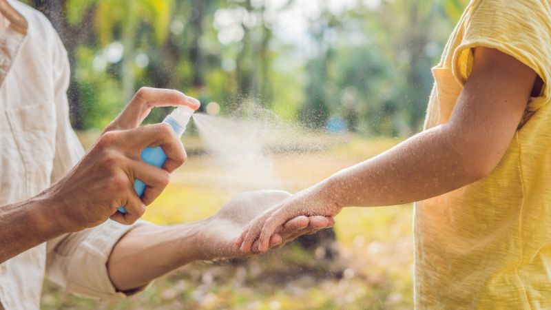frau besprüht den unterarm eins kindes mit insektenschutzmittel