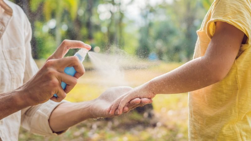 frau besprüht den unterarm eins kindes mit insektenschutzmittel