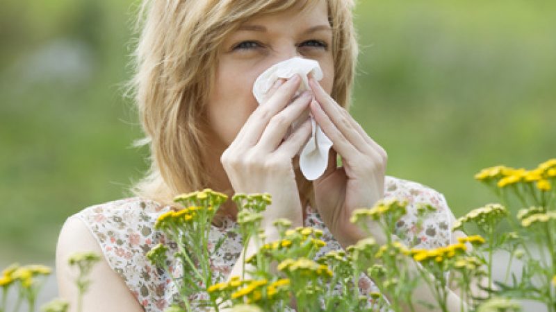 Young Caucasian woman blowing nose into tissue in front of flowers