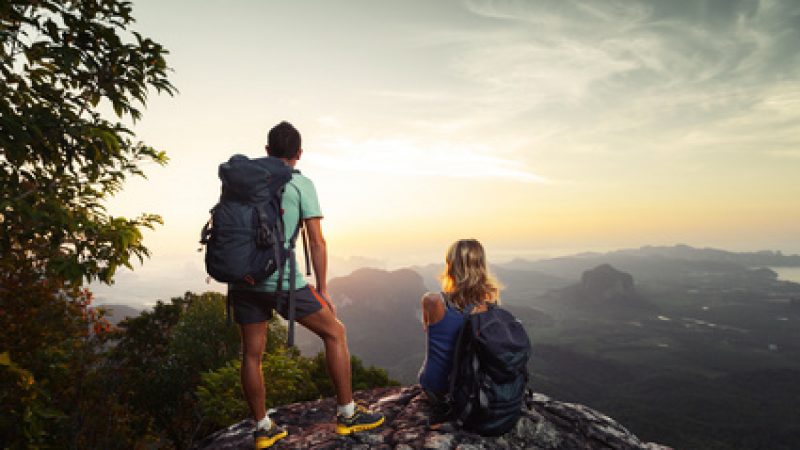 Two hikers relaxing on top of hill and enjoying sunrise over the valley